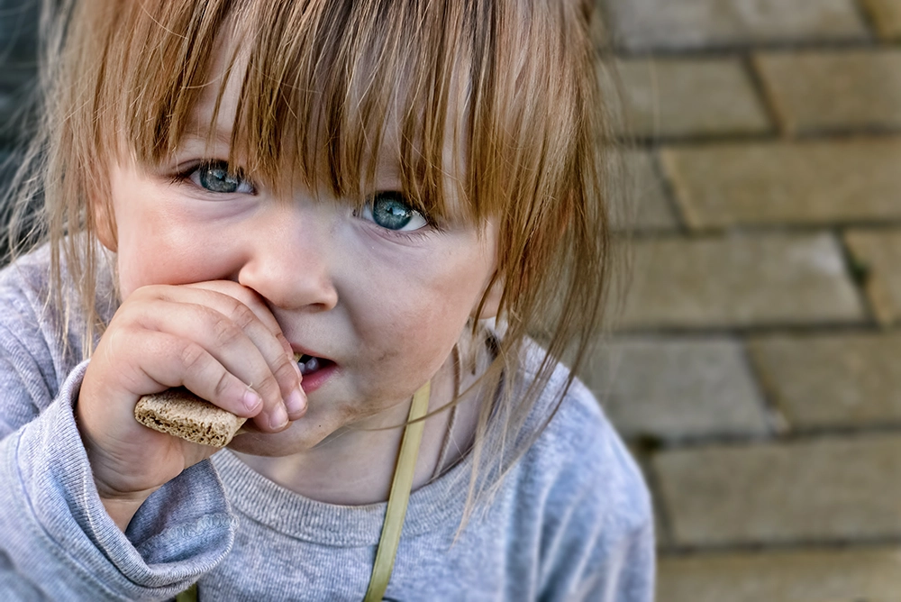 A poor girl eating a cracker.